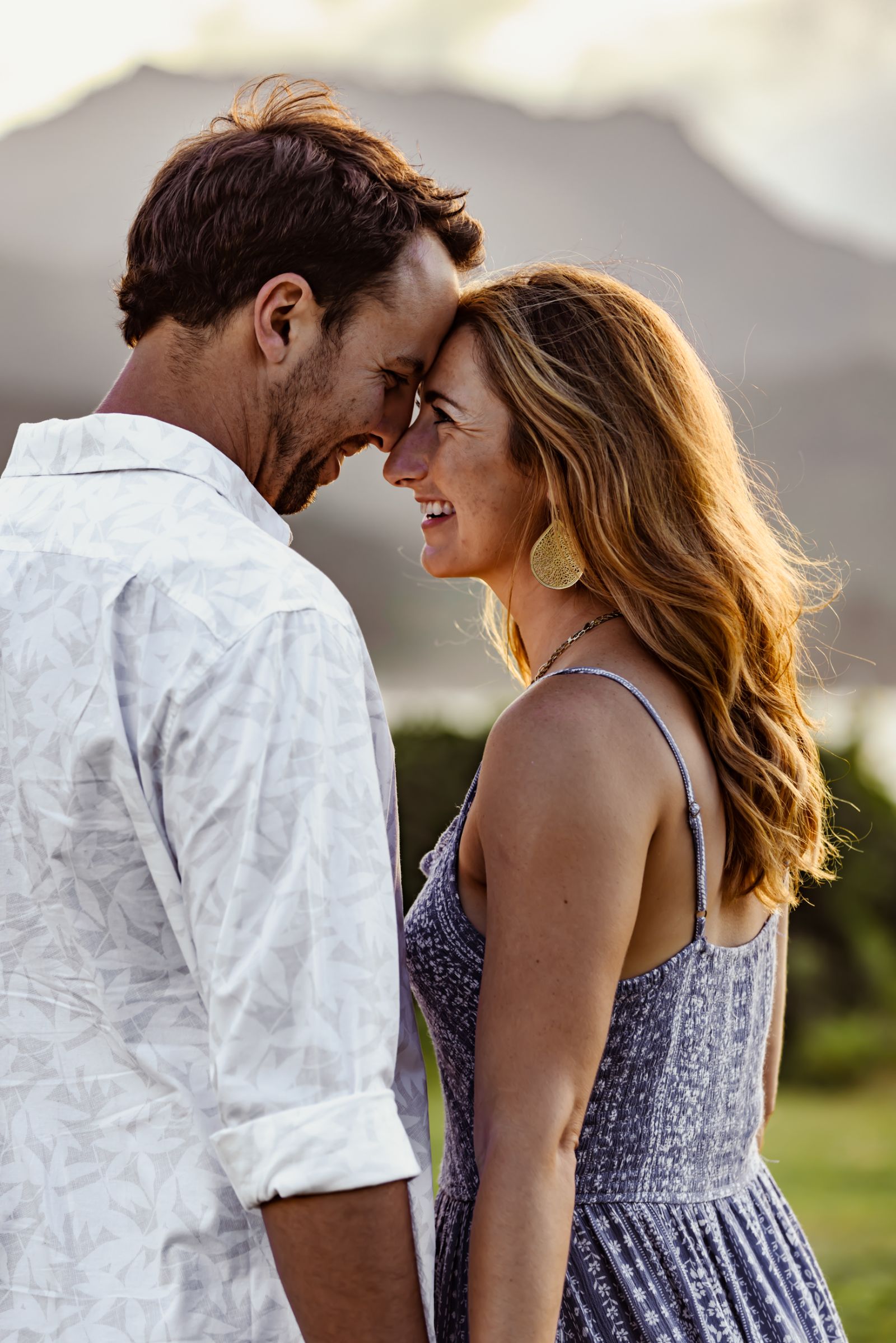 Engaged couple touching foreheads and laughing at golden hour with Hawaiian mountains behind them — engagement photography by Murrieta Media, serving Murrieta, Temecula and Southern California