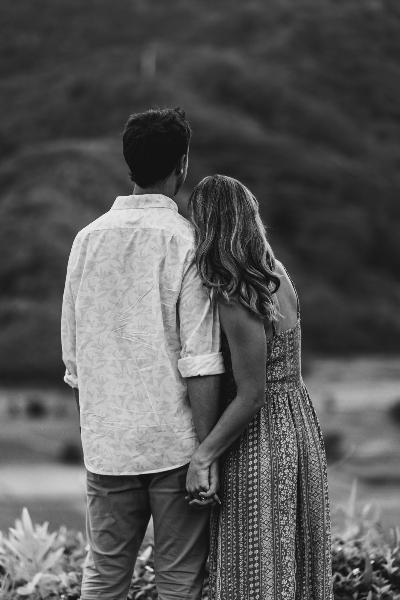Black and white photo of a couple holding hands from behind while looking out at the mountains — engagement photography by Murrieta Media