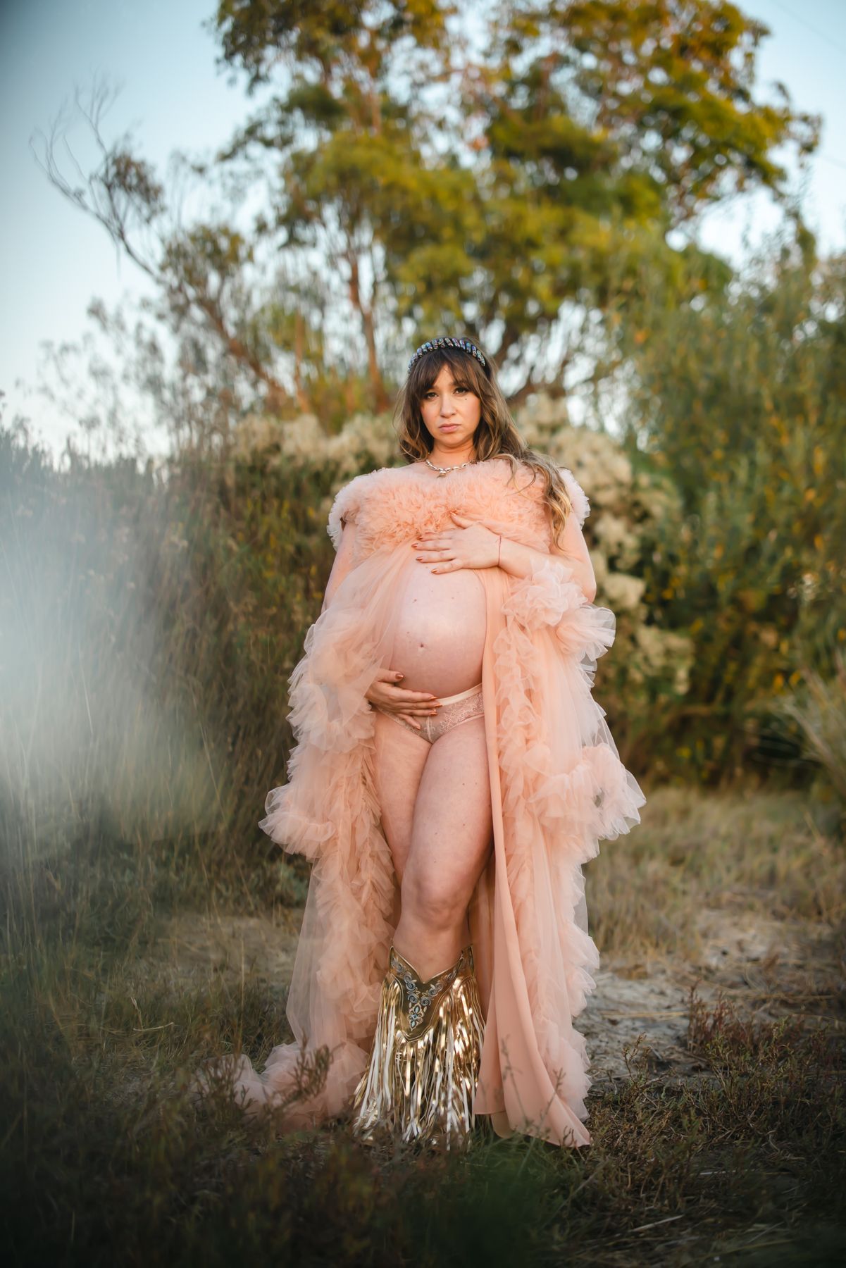 Maternity portrait of a mother in a flowing peach gown among wild greenery at sunset near Murrieta, California, by Murrieta Media