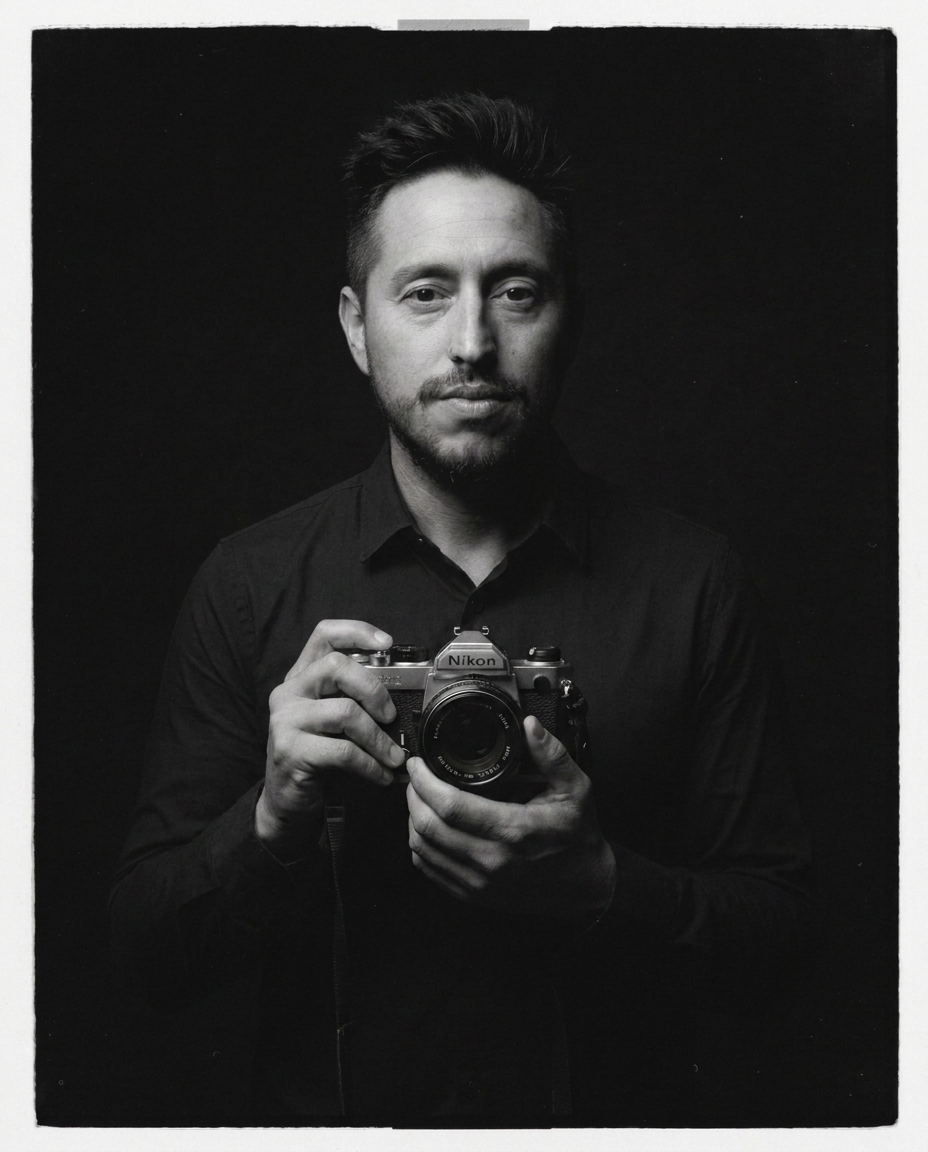 Black and white portrait of Jonathan Ramirez, founder of Murrieta Media, holding a vintage Nikon film camera — videographer and photographer in Murrieta and Temecula, Southern California