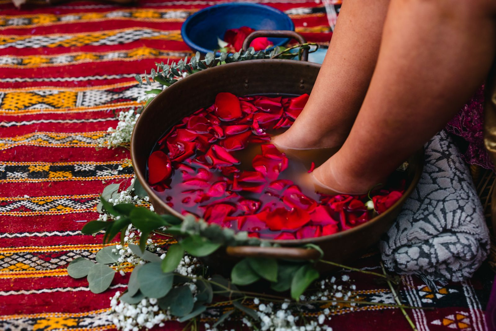 Bare feet soaking in a copper bowl of rose petals on a Moroccan rug during a blessingway ceremony, photographed by Murrieta Media